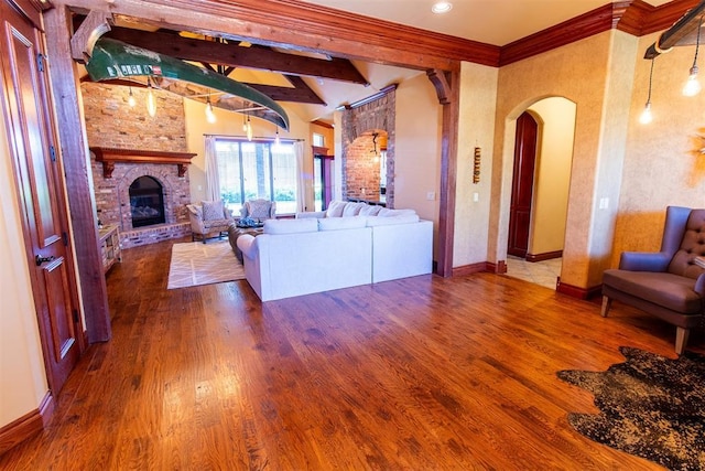 living room featuring beamed ceiling, hardwood / wood-style floors, a brick fireplace, and ornamental molding