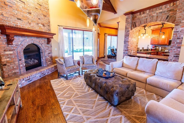 living room featuring sink, beam ceiling, light hardwood / wood-style flooring, a fireplace, and a chandelier