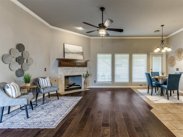 living room with wood-type flooring, ceiling fan with notable chandelier, a stone fireplace, and ornamental molding