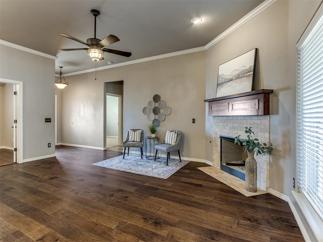 living area with ornamental molding, a brick fireplace, ceiling fan, and dark wood-type flooring