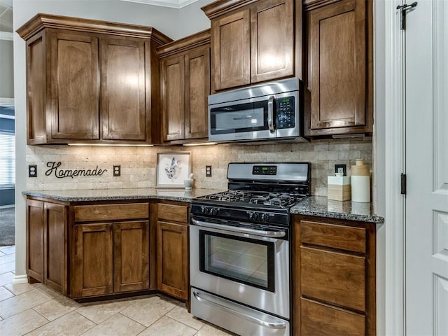 kitchen featuring stainless steel appliances, dark stone counters, decorative backsplash, light tile patterned floors, and ornamental molding