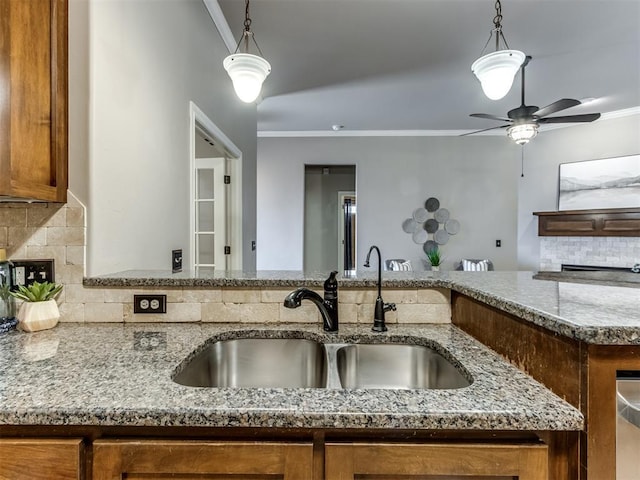 kitchen featuring backsplash, ornamental molding, ceiling fan, sink, and stone countertops