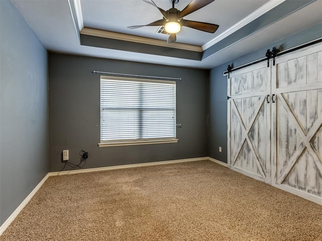 carpeted spare room with a barn door, a raised ceiling, ceiling fan, and crown molding