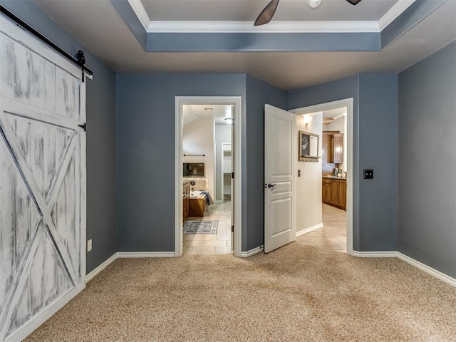 interior space with ceiling fan, a barn door, ornamental molding, a tray ceiling, and light colored carpet