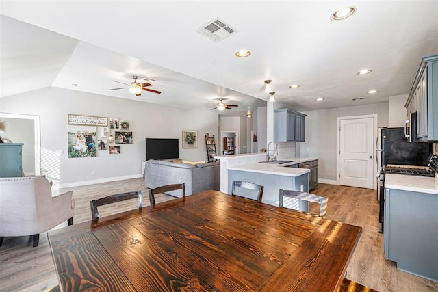 dining space featuring ceiling fan, sink, lofted ceiling, and light wood-type flooring