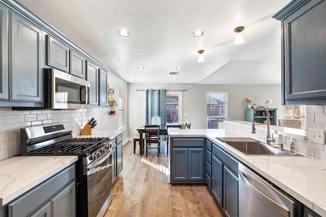 kitchen featuring sink, decorative backsplash, appliances with stainless steel finishes, light hardwood / wood-style floors, and kitchen peninsula