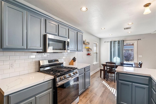 kitchen featuring light stone countertops, light hardwood / wood-style flooring, backsplash, gray cabinets, and appliances with stainless steel finishes