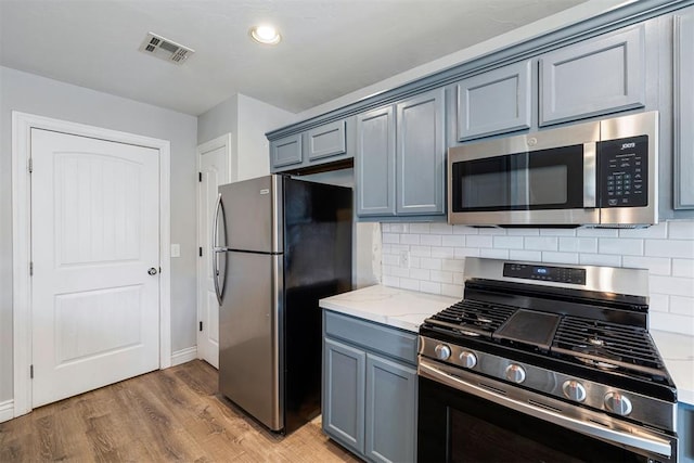 kitchen with appliances with stainless steel finishes, dark hardwood / wood-style flooring, tasteful backsplash, and light stone counters