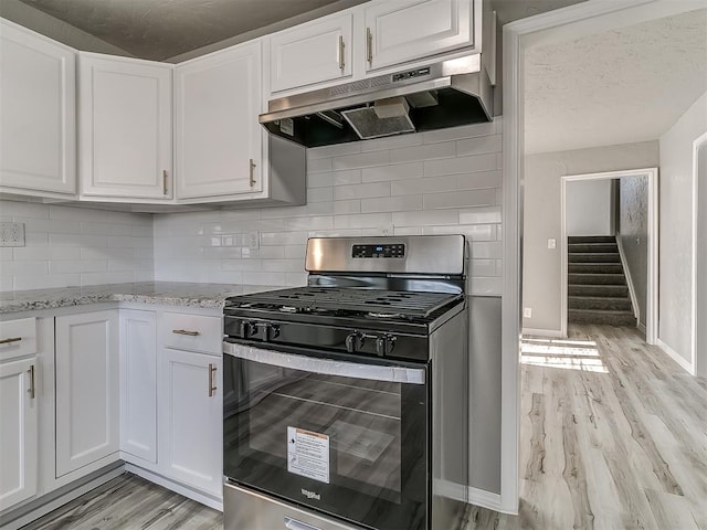 kitchen with light stone countertops, decorative backsplash, stainless steel gas stove, and white cabinetry