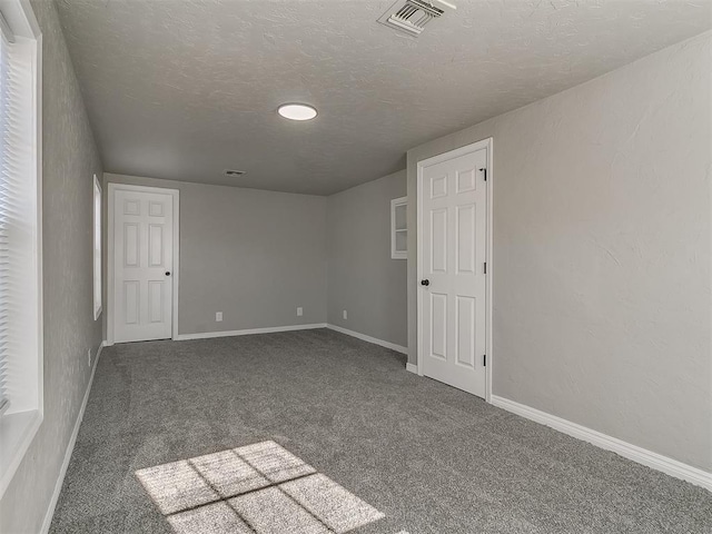 unfurnished room featuring a textured ceiling and dark carpet