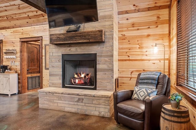 sitting room featuring a stone fireplace and wooden walls