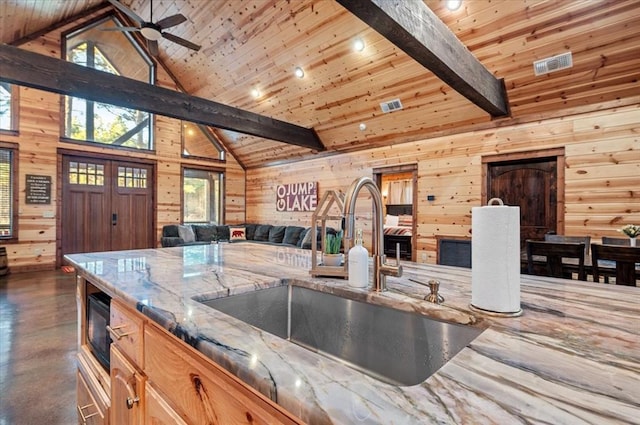 kitchen with beam ceiling, open floor plan, a sink, wooden walls, and wooden ceiling