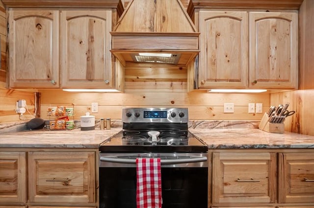 kitchen featuring light brown cabinets, wooden walls, light stone countertops, premium range hood, and stainless steel electric range