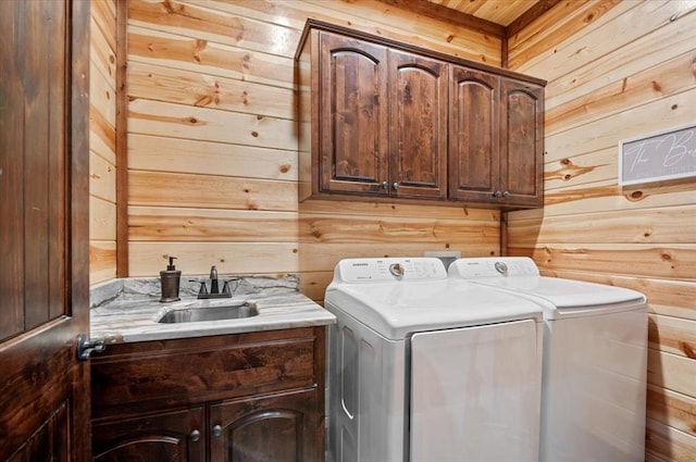 laundry area featuring a sink, wood walls, washing machine and clothes dryer, and cabinet space