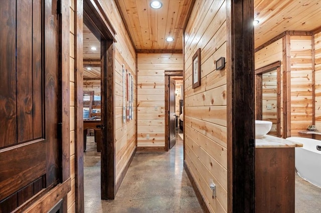 hallway featuring recessed lighting, concrete floors, wooden ceiling, and wooden walls