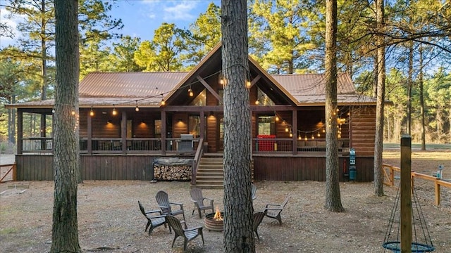 back of property featuring covered porch, stairs, a fire pit, and metal roof