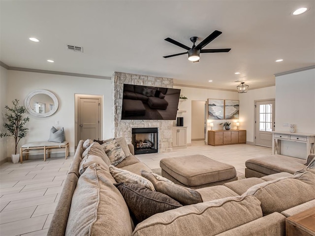 living room featuring ceiling fan, crown molding, and a stone fireplace