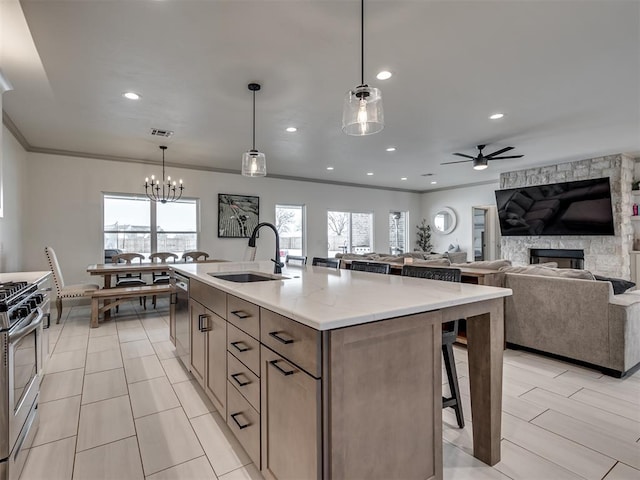 kitchen featuring stainless steel appliances, a fireplace, hanging light fixtures, sink, and an island with sink