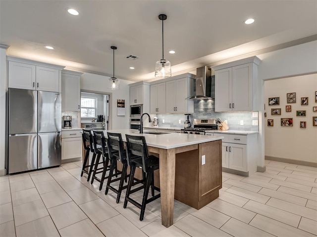 kitchen with wall chimney exhaust hood, stainless steel appliances, tasteful backsplash, hanging light fixtures, and a kitchen island with sink