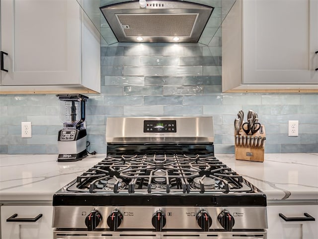 kitchen with light stone countertops, exhaust hood, white cabinetry, tasteful backsplash, and gas range