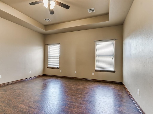 spare room featuring a raised ceiling, ceiling fan, and dark hardwood / wood-style flooring