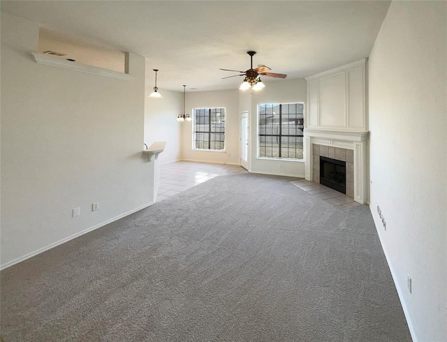 unfurnished living room with a fireplace, light colored carpet, and ceiling fan with notable chandelier