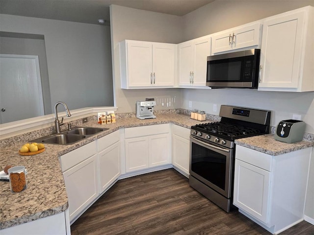 kitchen with appliances with stainless steel finishes, light stone counters, sink, white cabinets, and dark hardwood / wood-style floors