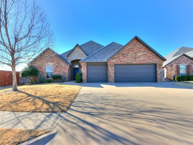 view of front facade with fence, a shingled roof, concrete driveway, a garage, and brick siding