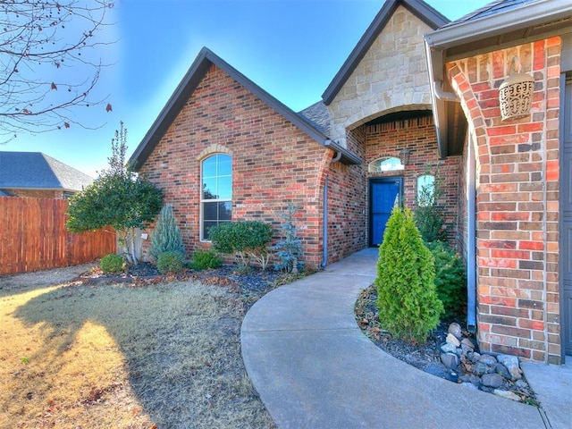 entrance to property featuring brick siding, stone siding, and fence