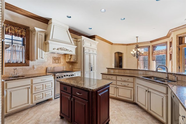 kitchen featuring high end stainless steel range oven, premium range hood, cream cabinets, and sink