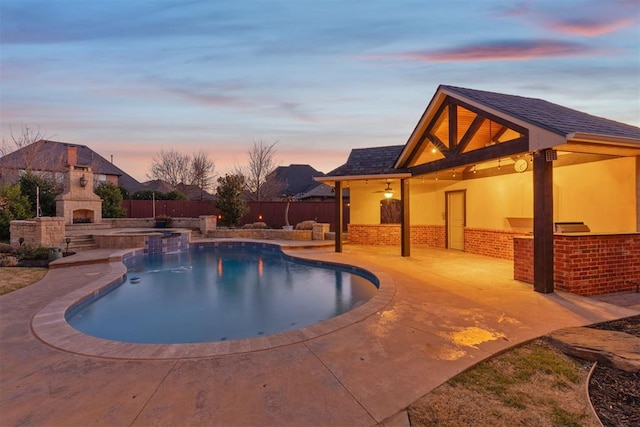 pool at dusk with an outdoor fireplace and a patio area