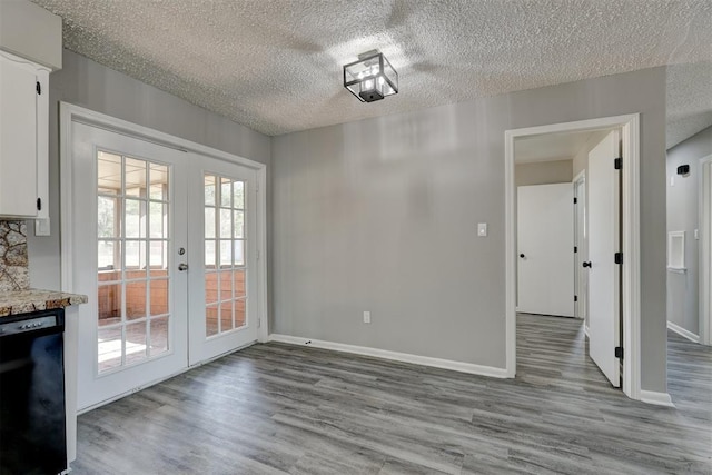 unfurnished dining area with french doors, a textured ceiling, and light hardwood / wood-style floors