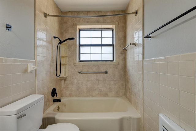 bathroom with tiled shower / bath, toilet, and tile walls