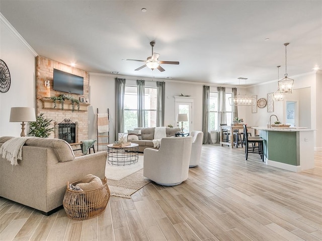 living room featuring ceiling fan with notable chandelier, light hardwood / wood-style floors, crown molding, and a brick fireplace