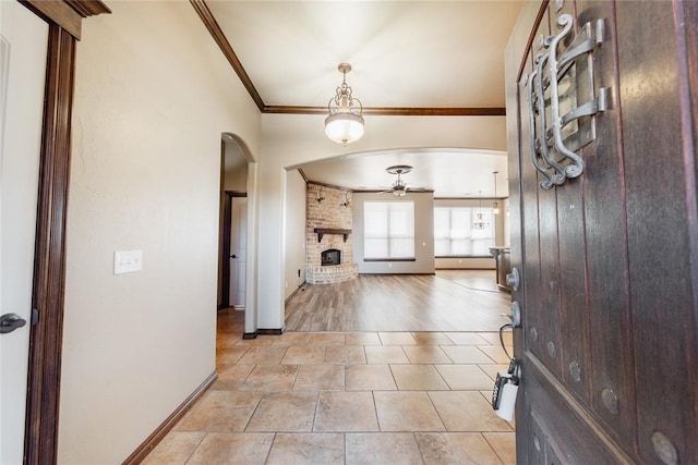 entryway with a brick fireplace, ceiling fan, and crown molding