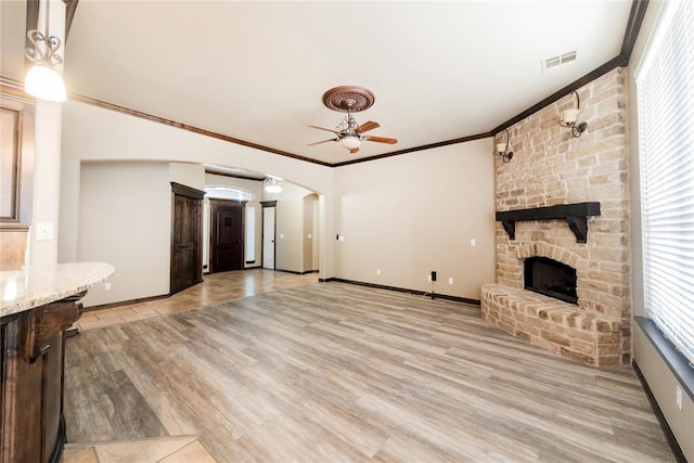 unfurnished living room featuring a fireplace, ceiling fan, light wood-type flooring, and ornamental molding