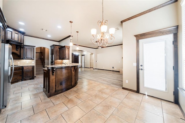 kitchen featuring a kitchen island with sink, stainless steel refrigerator, pendant lighting, dark brown cabinetry, and an inviting chandelier