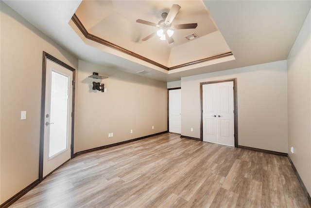 unfurnished bedroom with ceiling fan, a tray ceiling, ornamental molding, and light hardwood / wood-style flooring