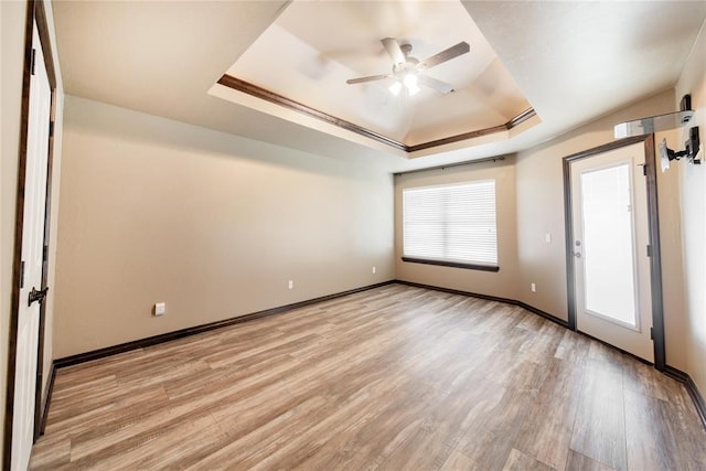 empty room featuring light hardwood / wood-style floors, ceiling fan, crown molding, and a tray ceiling