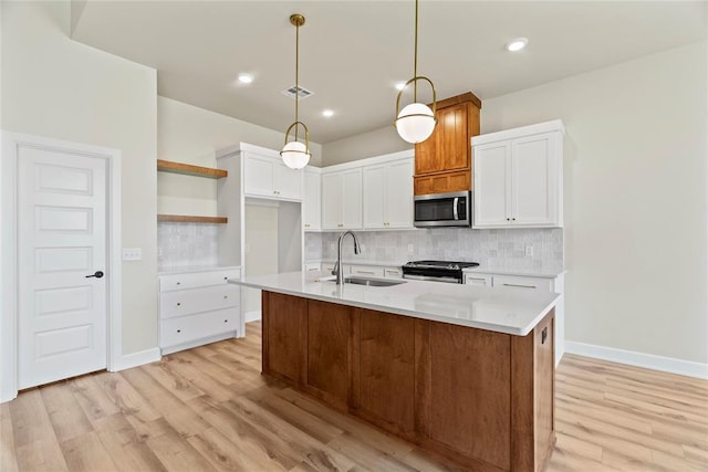 kitchen featuring stainless steel appliances, sink, decorative light fixtures, a center island with sink, and white cabinetry