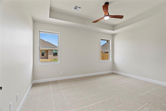 spare room featuring a raised ceiling, ceiling fan, and light carpet