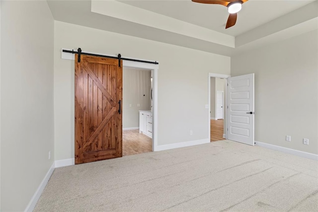 unfurnished bedroom featuring carpet flooring, connected bathroom, ceiling fan, a raised ceiling, and a barn door