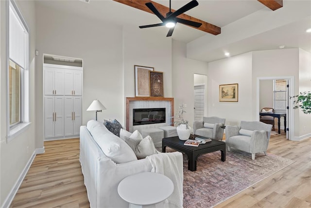 living area featuring baseboards, ceiling fan, beamed ceiling, light wood-type flooring, and plenty of natural light