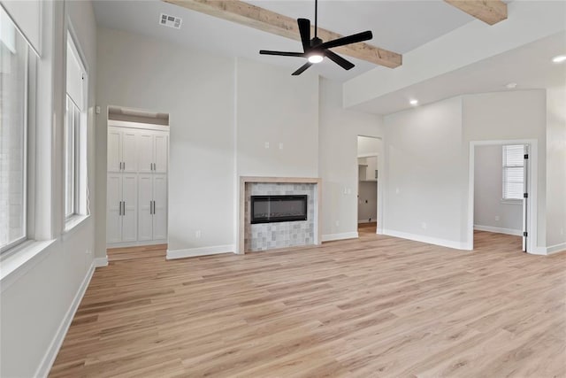 unfurnished living room with a tile fireplace, ceiling fan, beamed ceiling, and light hardwood / wood-style floors