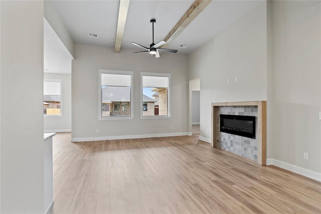 unfurnished living room featuring beam ceiling, light hardwood / wood-style flooring, ceiling fan, and a tiled fireplace