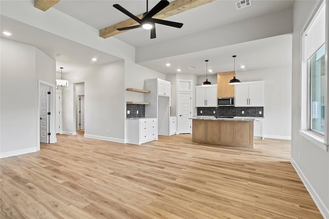 kitchen featuring a kitchen island with sink, ceiling fan, decorative light fixtures, beamed ceiling, and white cabinetry