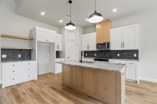 kitchen with sink, stainless steel appliances, an island with sink, decorative light fixtures, and white cabinets