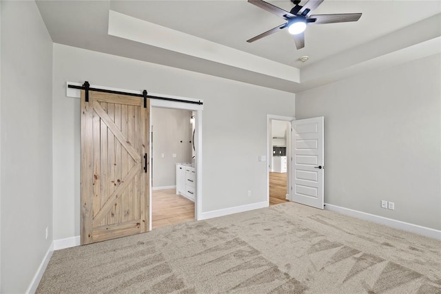 unfurnished bedroom featuring a tray ceiling, a barn door, ceiling fan, and connected bathroom