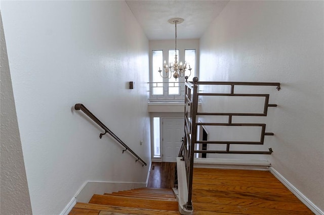 stairs featuring wood-type flooring and a notable chandelier