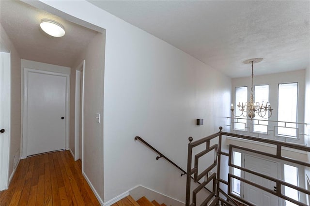 staircase with wood-type flooring, a notable chandelier, and a textured ceiling